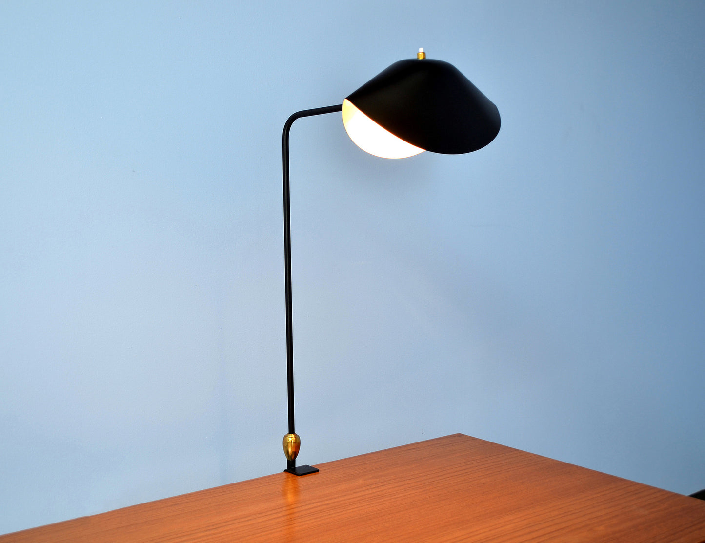 Black Serge Mouille Agrafee Desk Lamp clamped to a desk on blue background