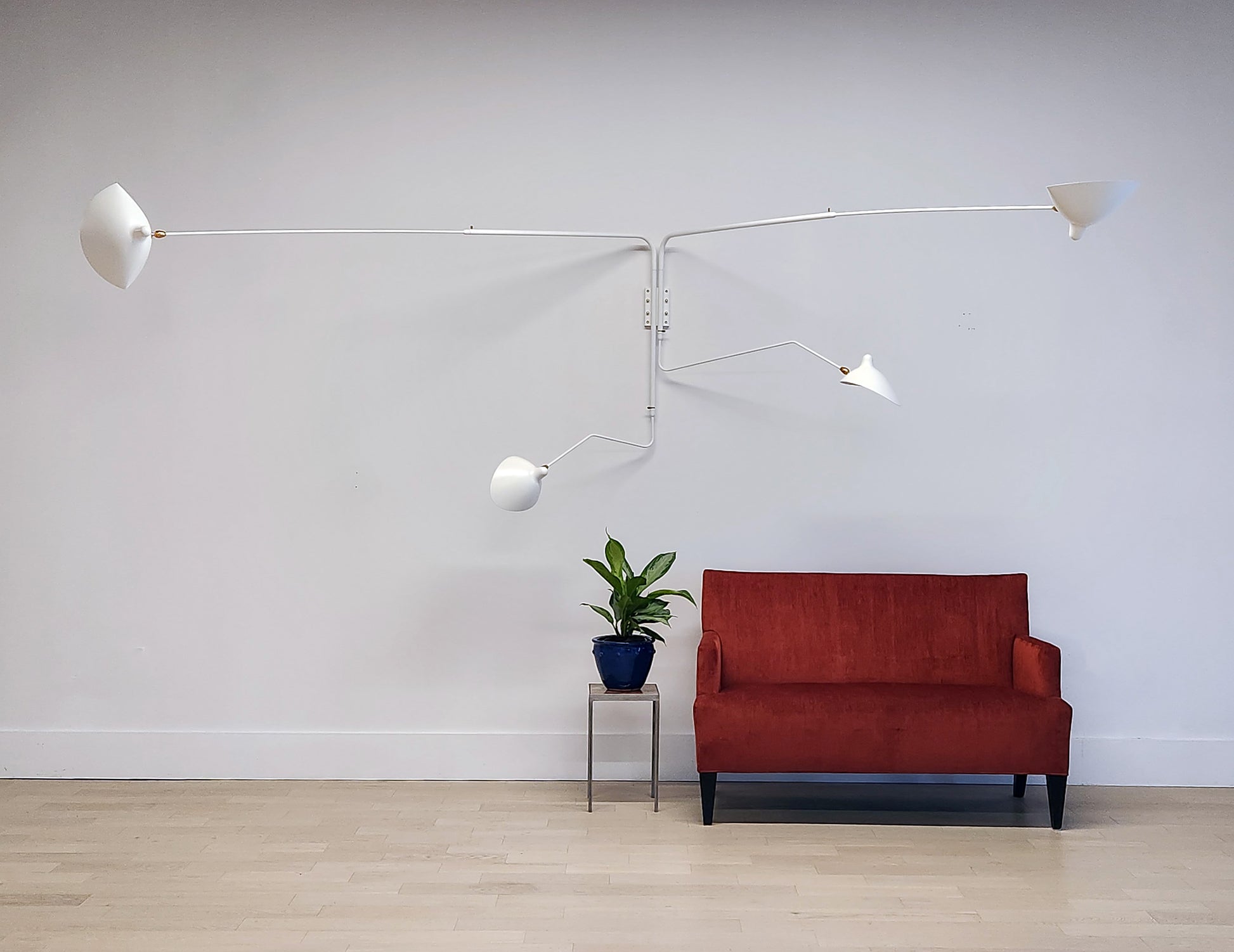 White Serge Mouille Rotating Sconce with 4 Arms with red sofa and plant