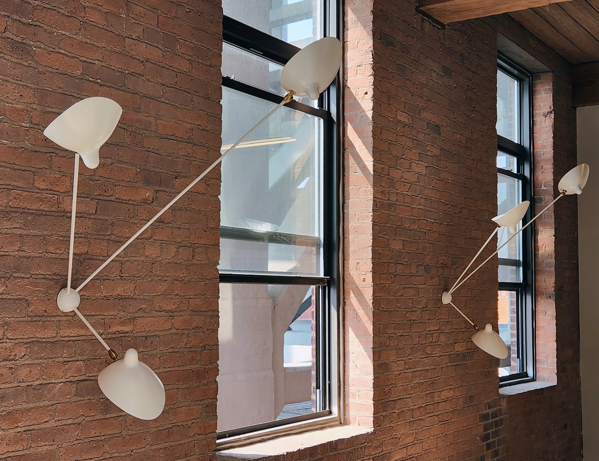 Pair of white Serge Mouille Spider Sconce with 3 Arms on a brick wall