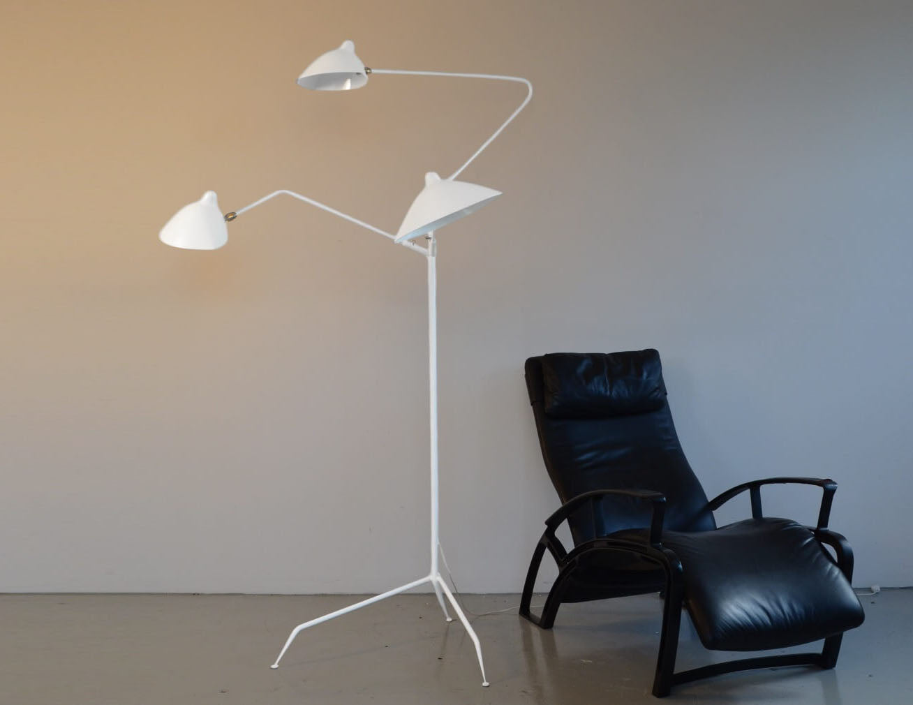 White Serge Mouille Floor Lamp with 3 Arms next to a black reclining chair